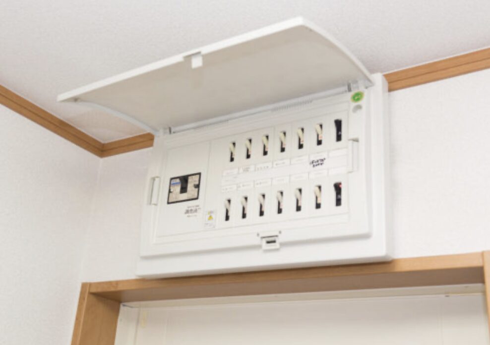 天井付近の壁面に設置された分電盤のカバーが開いた状態。複数のブレーカーが並ぶ住宅用配電盤の様子。