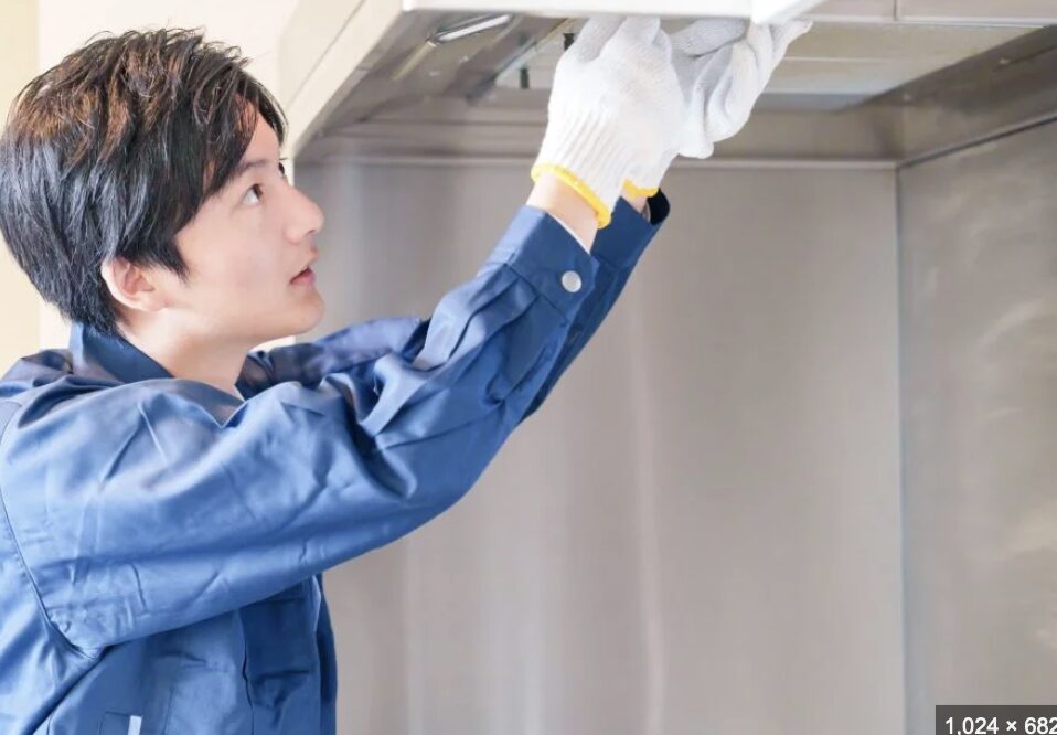作業服を着た男性がレンジフード内部の部品を点検している様子。
