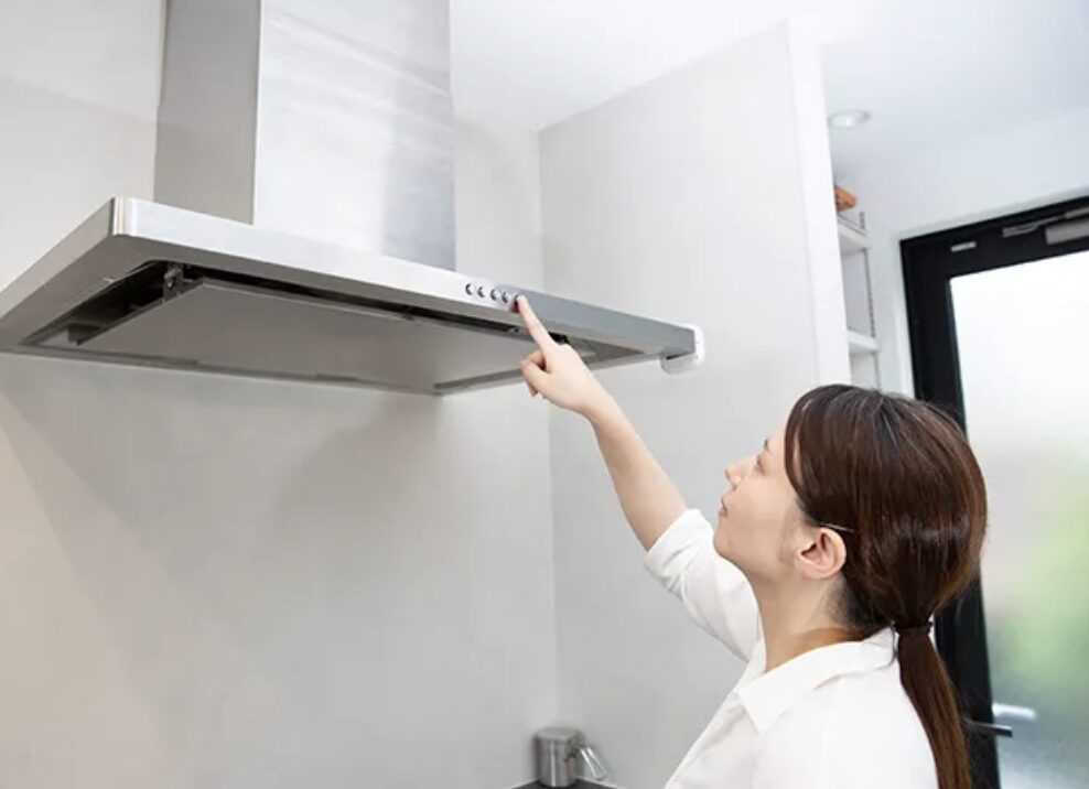 キッチンのスリム型レンジフードの操作ボタンを押している女性の様子。