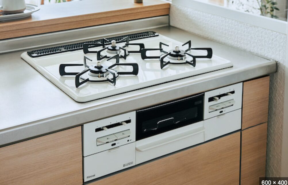 木目キャビネットに組み込まれた白い天板のビルトインガスコンロ。三口バーナーと中央グリルを備えたシンプルな住宅用キッチン設備。