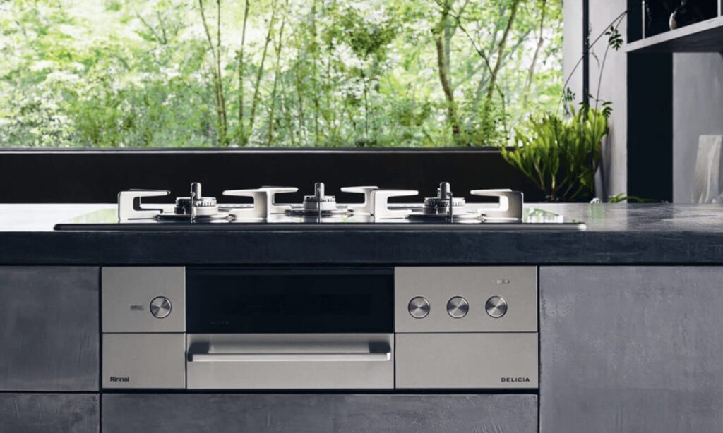 モダンなキッチンに設置されたビルトインガスコンロの写真。大きな窓の外に緑が広がり、ステンレス天板とシルバーの操作パネルが映えるデザイン。