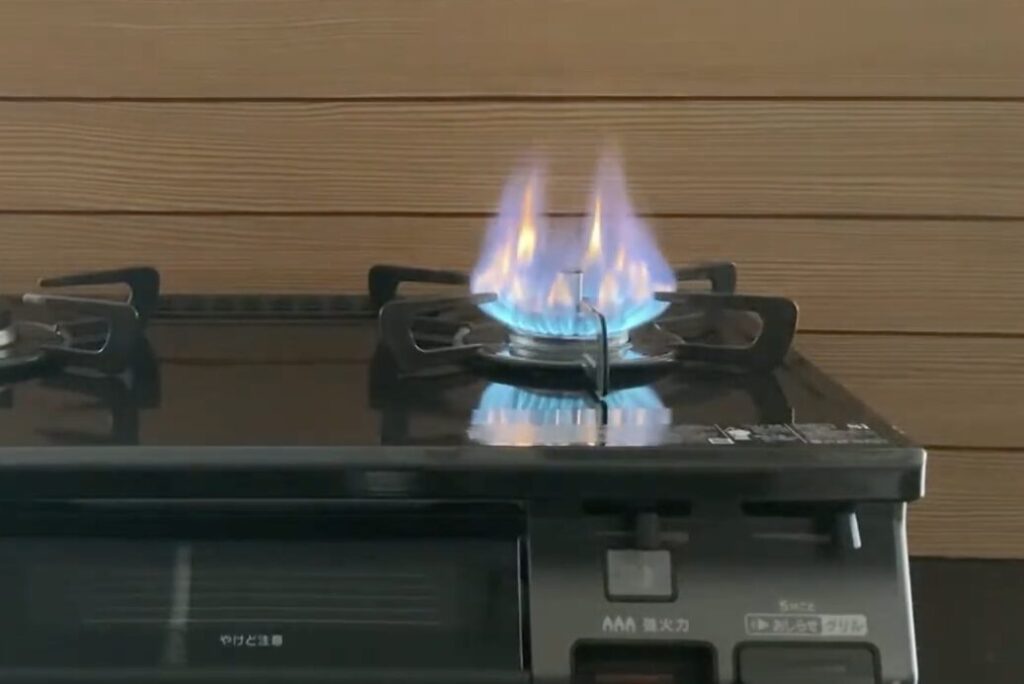 家庭用ガステーブルのバーナーに青い炎が立ち上がっている燃焼状態のクローズアップ。