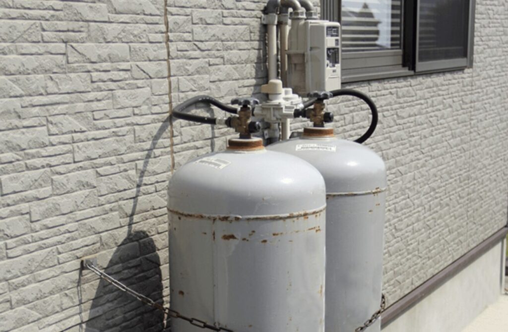 レンガ調の外壁に並んで設置されたLPガス容器2本と調整器・ガスメーターの接続部分の様子。