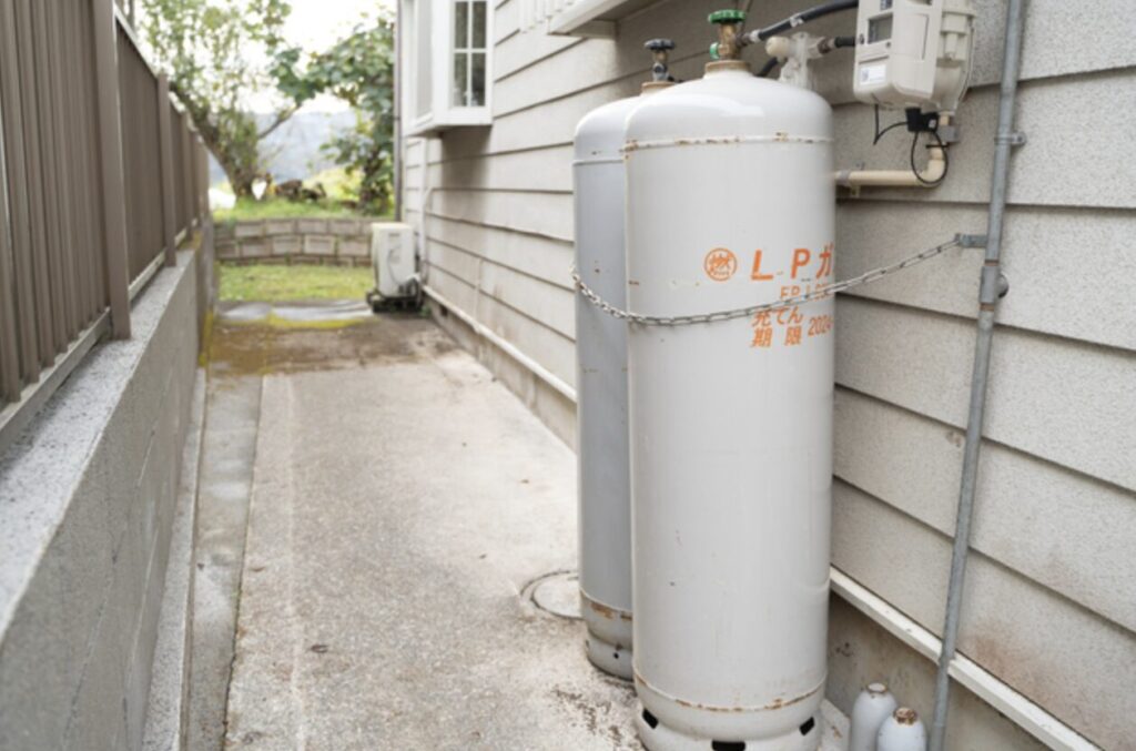 住宅の外壁沿いに鎖で固定されたLPガスボンベ2本とガスメーターが設置されている屋外設置状況。