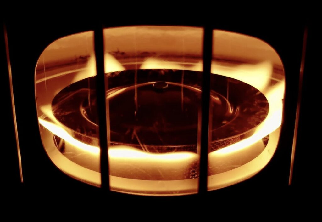 燃焼中の石油ストーブ内部を写した写真。円形のバーナー部分がオレンジ色に発光し、炎が広がっている様子。