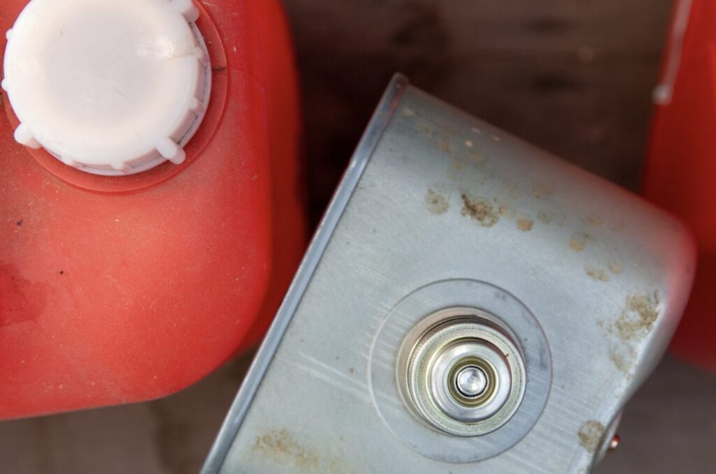 赤いポリタンクの注ぎ口付近と、金属製の灯油タンク上部を写した写真。給油口や金属部分に汚れやサビが見られる。