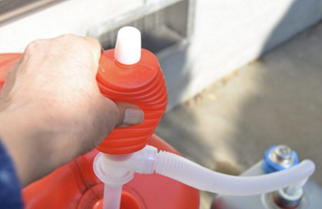 赤い灯油ポリタンクに手動ポンプを差し込み、灯油を移している様子の写真。手でポンプ上部を押して給油している場面。