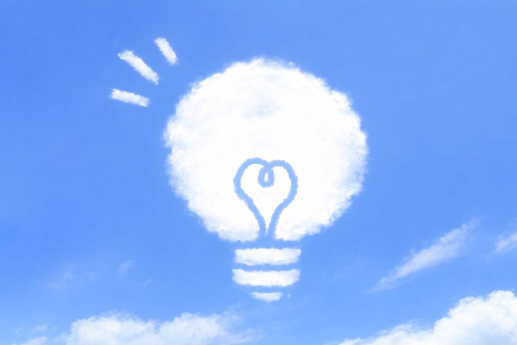 青空に雲で描かれた電球の形とハート型フィラメントが浮かぶイメージイラスト