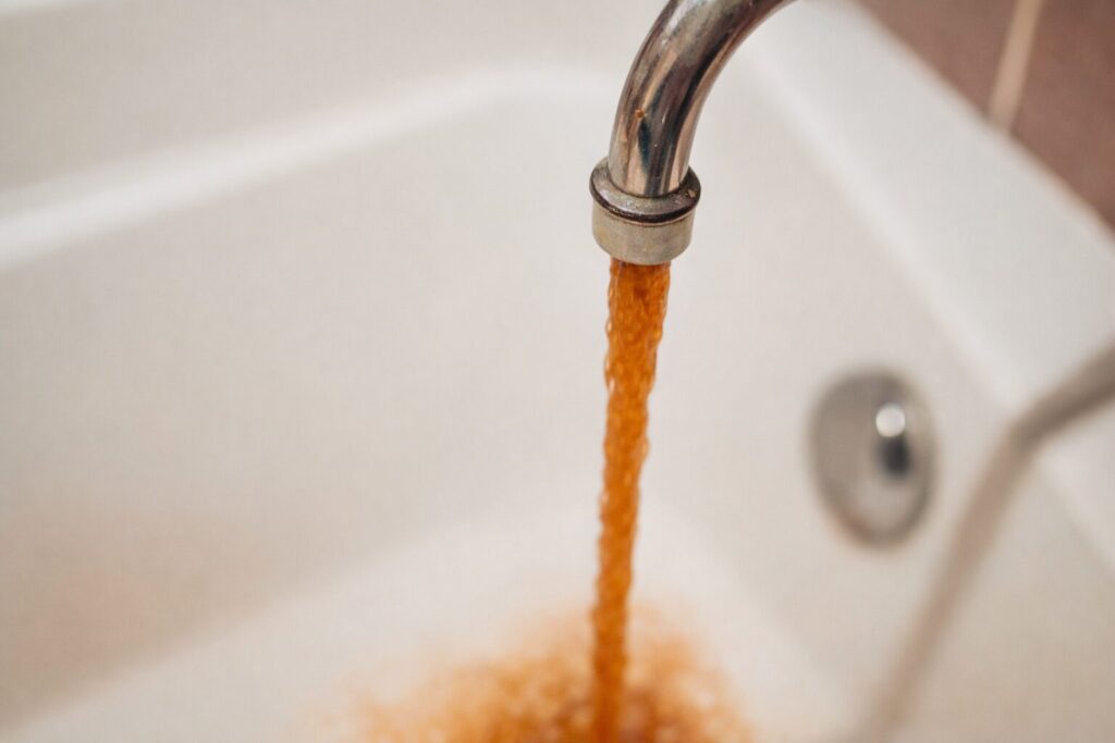 蛇口から赤錆の影響で茶色く濁った水が流れ出ている様子