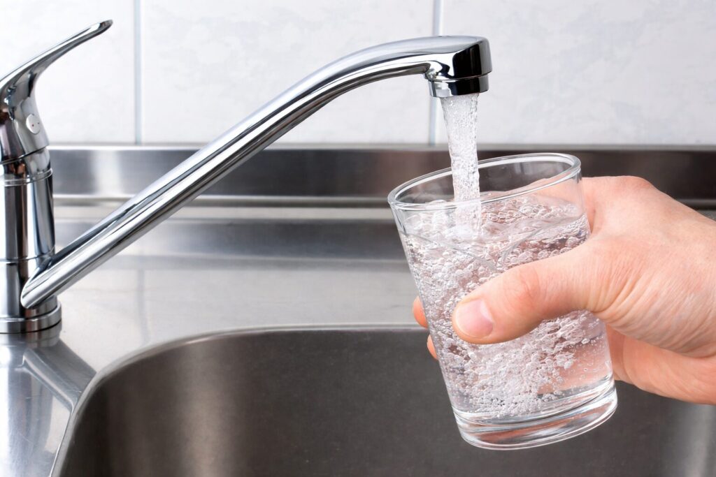 キッチンの蛇口から透明な水が流れ、手に持ったコップに注がれている様子