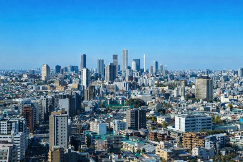 高層ビル群と住宅街が広がる都市の全景を、青空の下から見渡したパノラマ風景