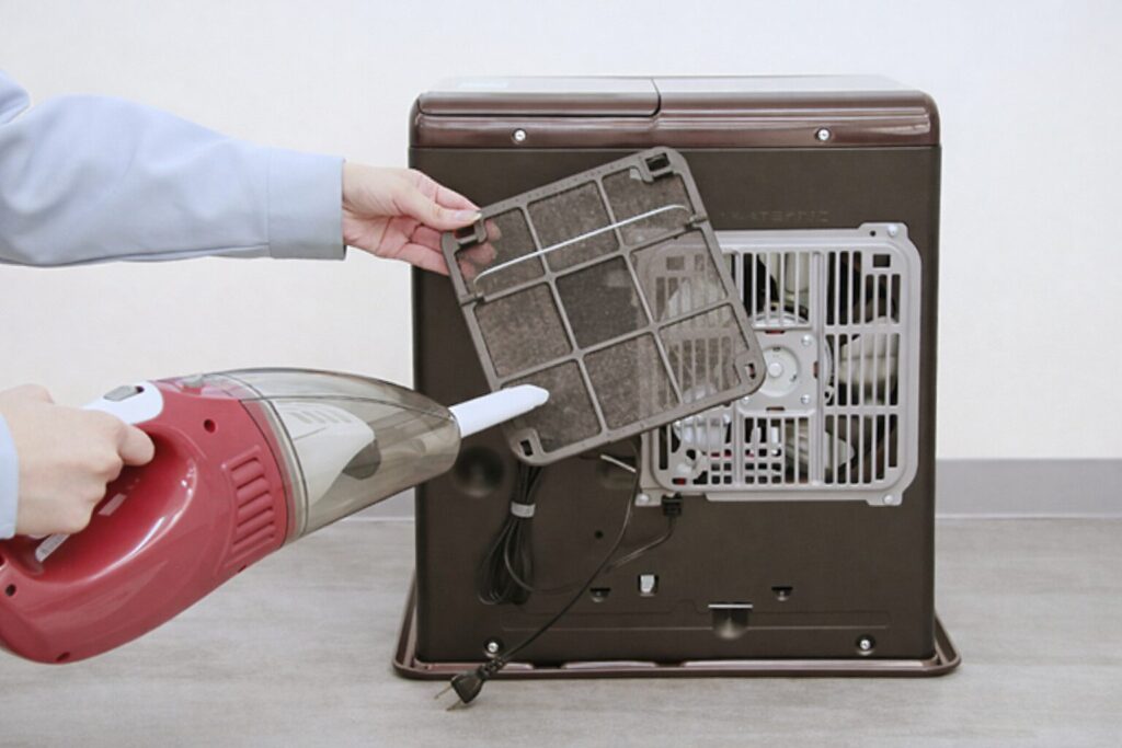 ヒーターの背面フィルターを取り外し、ハンディ掃除機でホコリを吸い取って清掃している様子