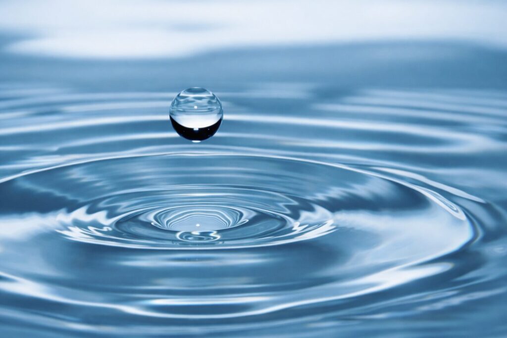 水面に落ちる直前の水滴と、広がる波紋を捉えた高精細なイメージ