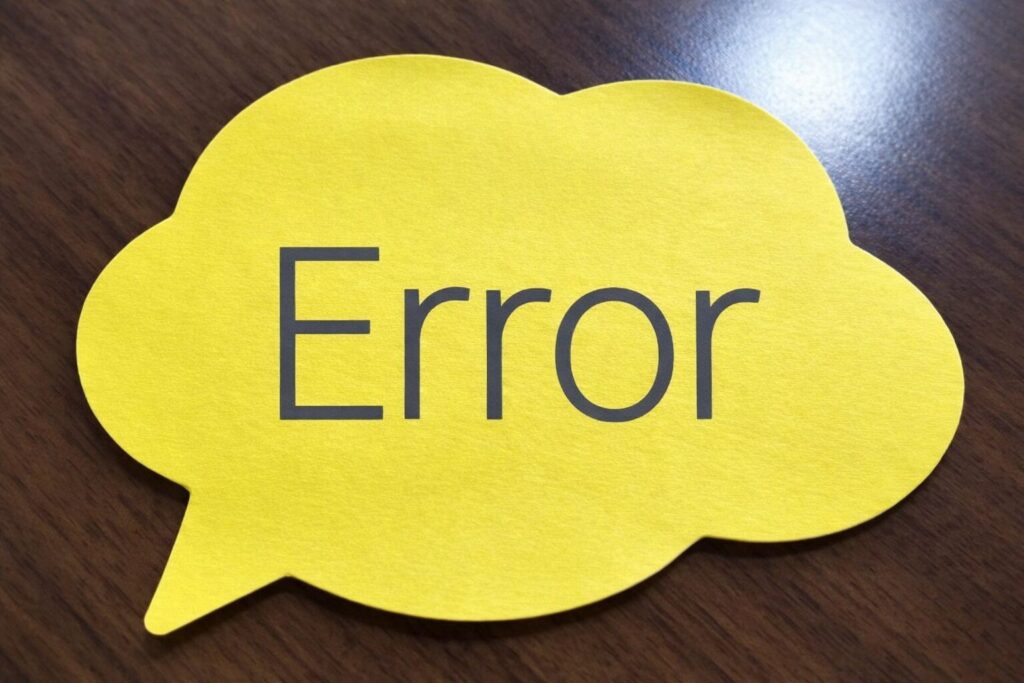 木目のテーブルの上に置かれた黄色い吹き出し型の紙に「Error」と書かれている様子
