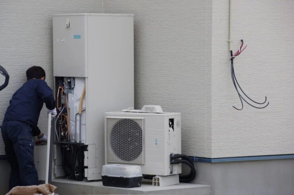 住宅の外壁横に設置されたエコキュート本体を作業員が点検している様子