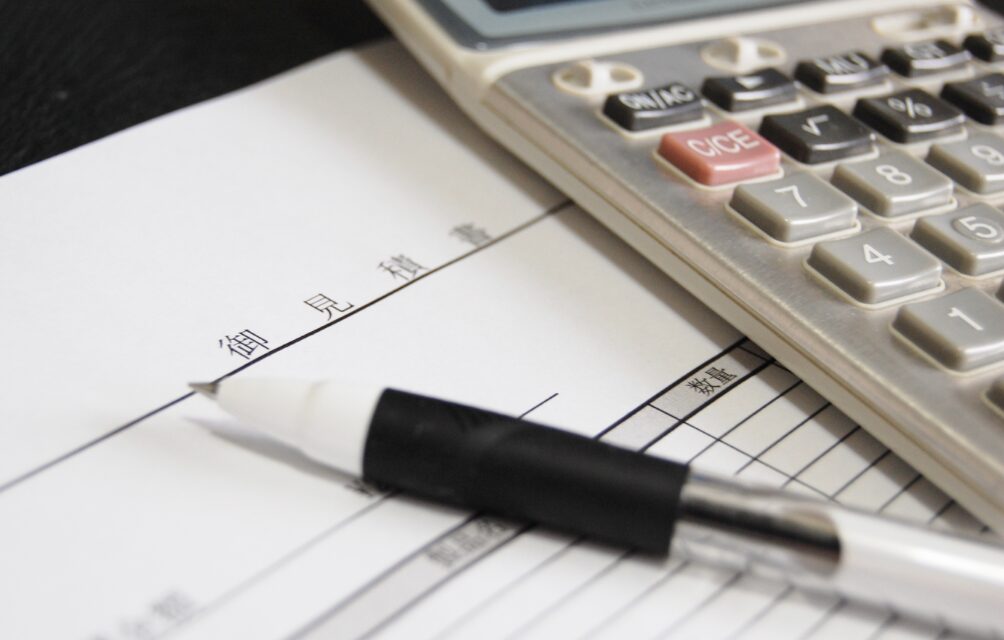 見積書と書かれた書類の上に電卓とボールペンが置かれている様子