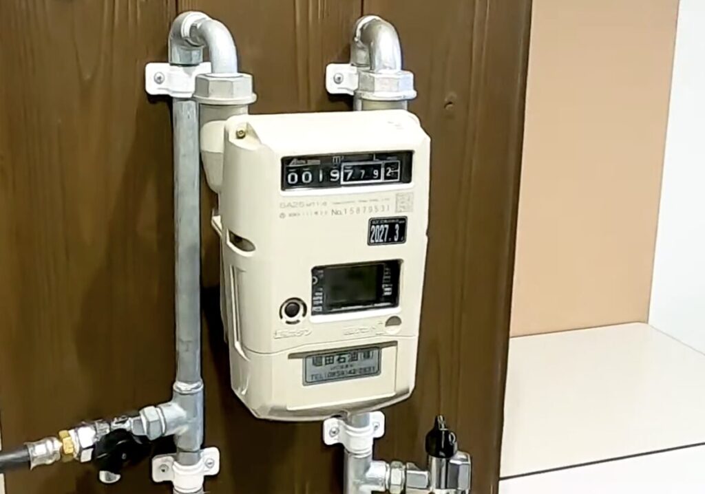 屋内に設置されたガスメーター本体と配管の様子。金属管とバルブが接続され、使用量表示窓が確認できる。