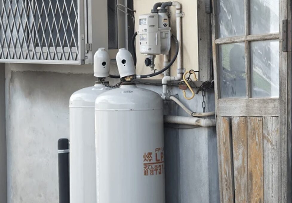 LPガスボンベが2本並んで設置され、調整器や配管が接続された住宅外壁のガス供給設備の様子