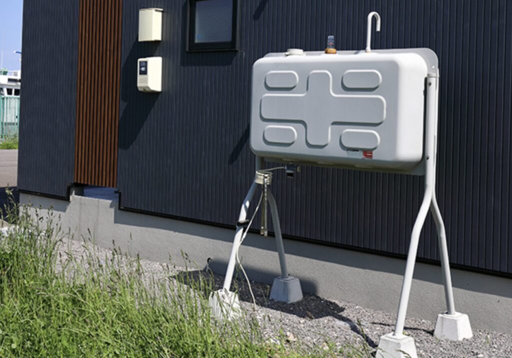 住宅外壁の横に設置された脚付きの屋外灯油タンクと給油配管の様子