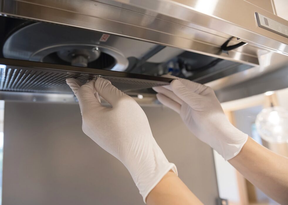 キッチンのレンジフードフィルターを手袋をつけて取り外している様子
