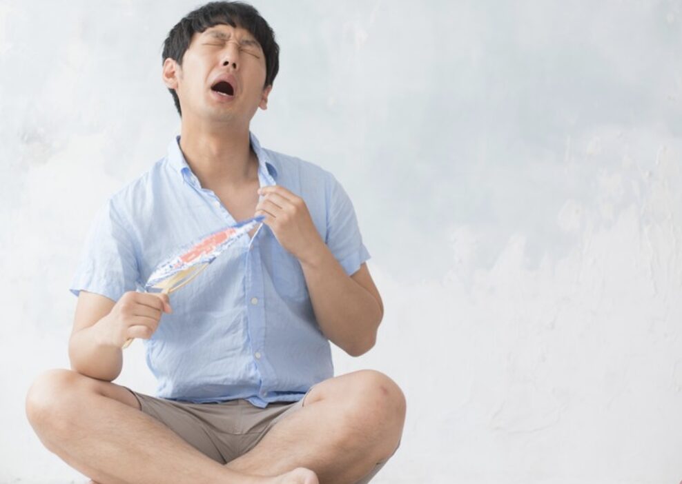 暑さで汗をかきながらうちわであおいでいる男性の様子