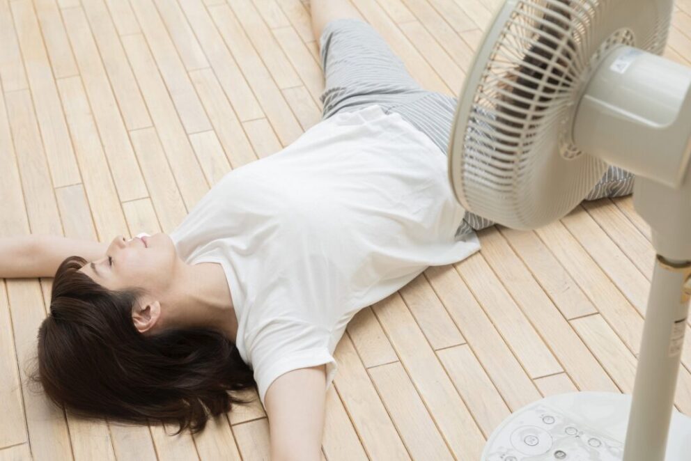 扇風機の前で暑さに疲れて床に寝転んでいる女性