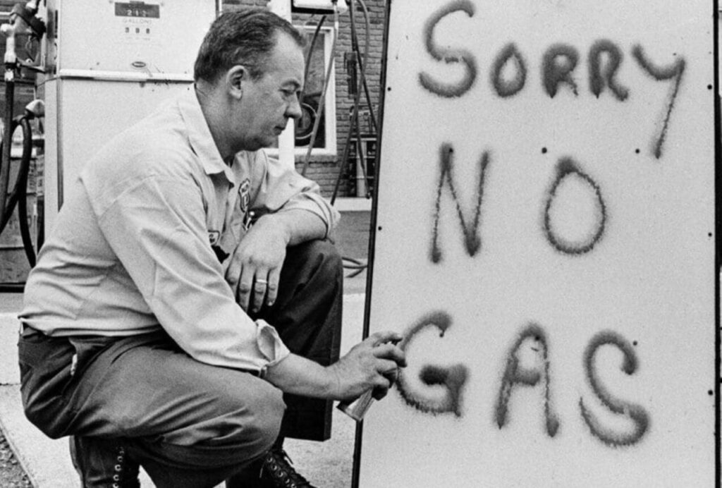 ガソリンスタンドの前で「SORRY NO GAS」と書かれた看板にスプレーで文字を書く男性の様子