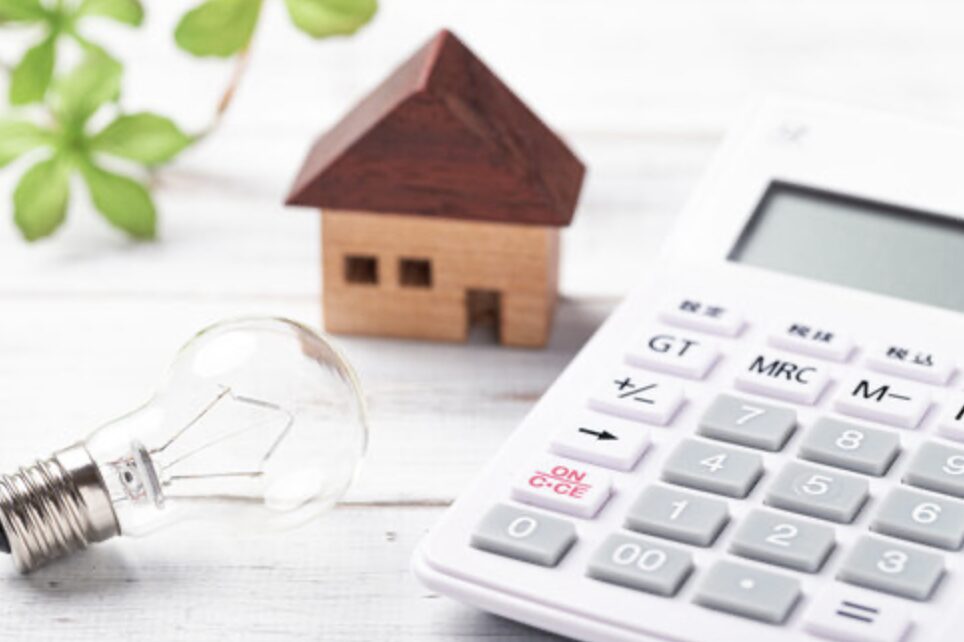 電卓と電球、家の模型が並び、光熱費や電気代など住宅のエネルギーコストをイメージした写真