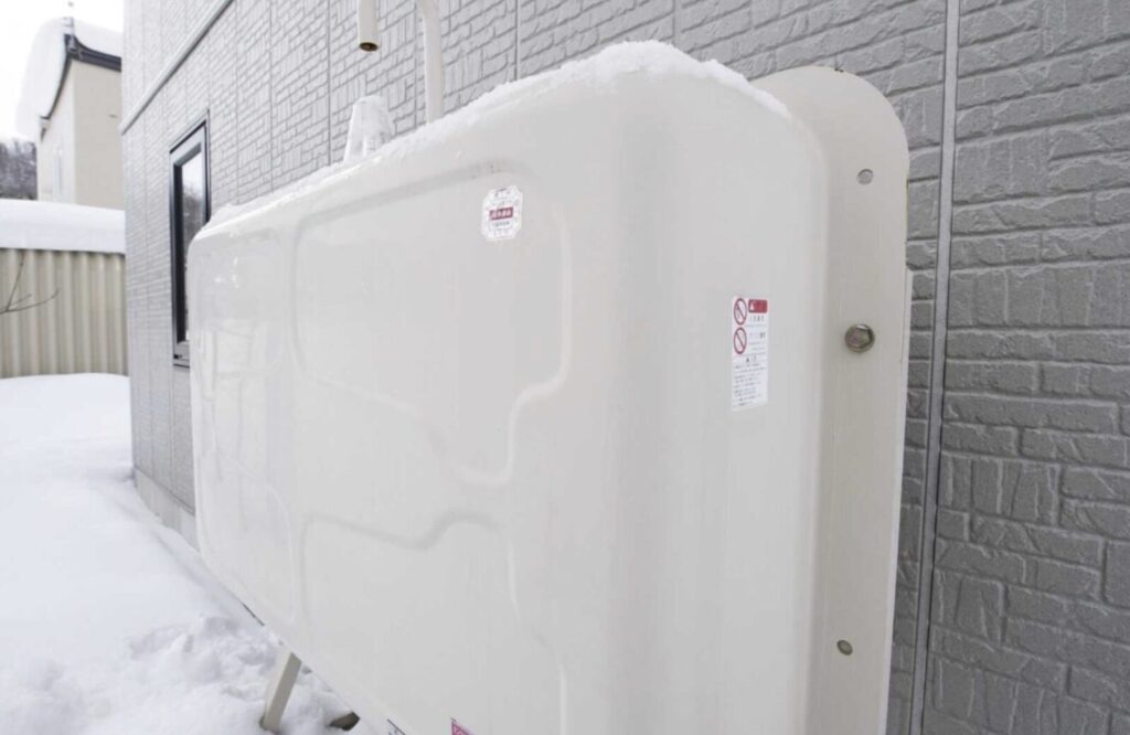 住宅の外壁横に設置された大型の灯油タンクと積もった雪のある冬の屋外設備