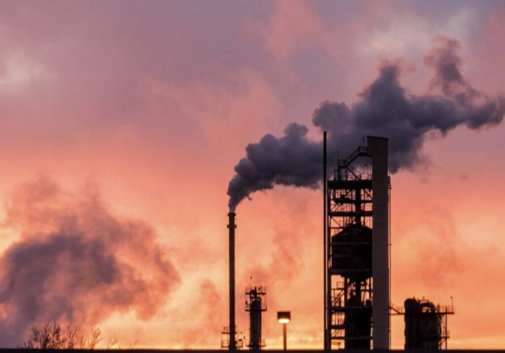 夕焼け空を背景に煙を排出する石油プラントの煙突と工業設備