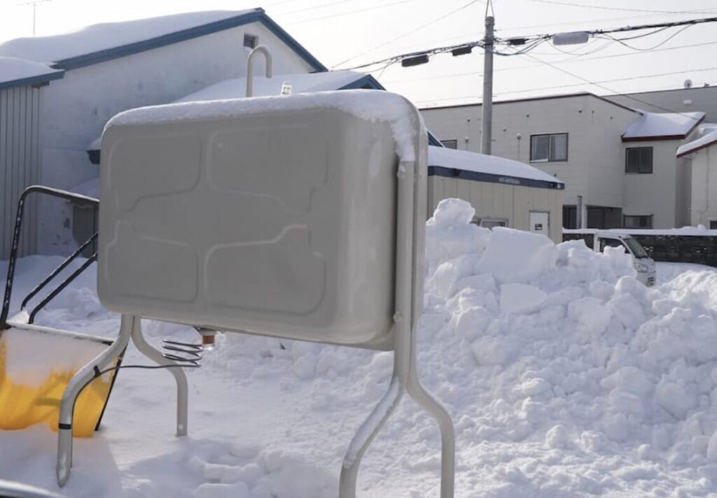 雪が積もった屋外設置の灯油タンクと住宅周辺の様子