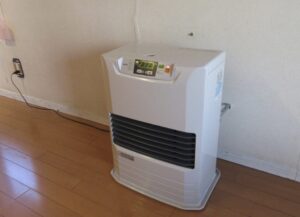 室内の壁際に設置された白い石油ファンヒーターが床の上に置かれている様子の写真