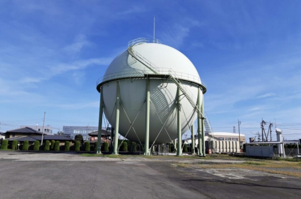 青空の下に立つ球形の都市ガスガスホルダー設備と周囲の住宅地の風景