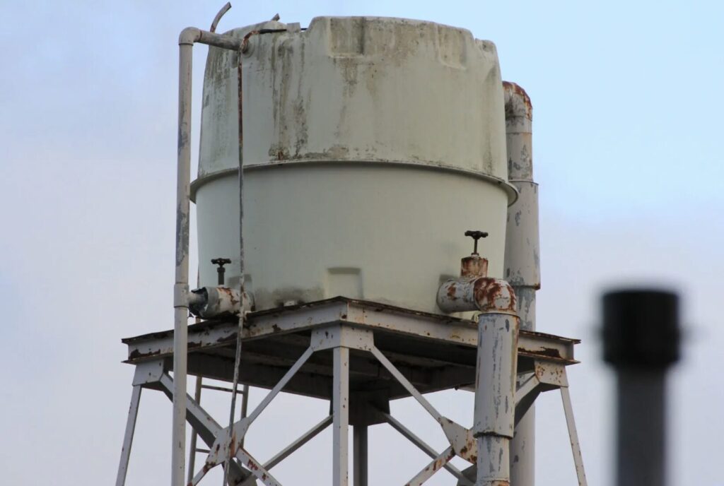 屋外に設置された錆びが見られる高架水槽と配管設備の様子