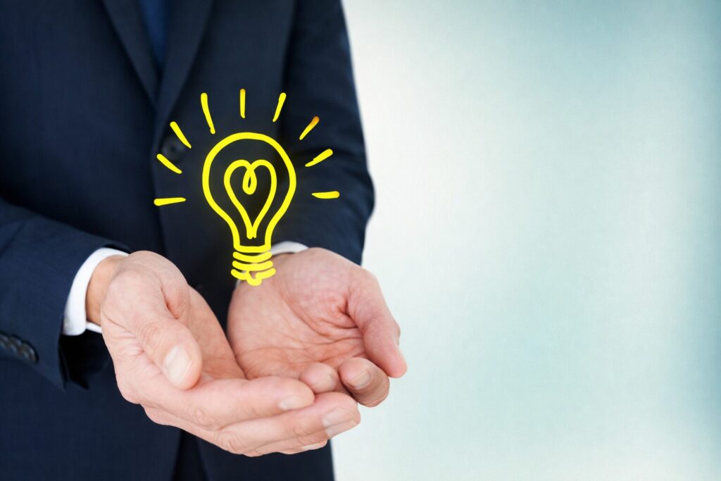 手のひらの上に光る電球のイラストが浮かび、アイデアや発想を表現しているビジネスイメージ