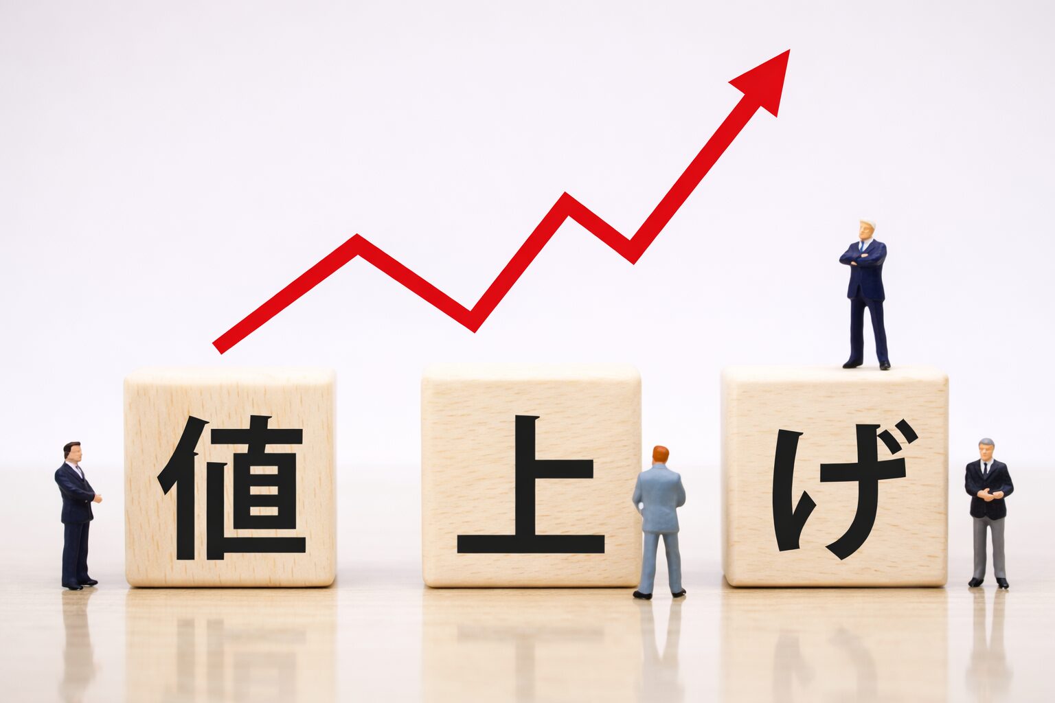 値上げを示す木製ブロックと上昇する赤い矢印を背景に、ビジネス人物のミニチュアが配置されたイメージ