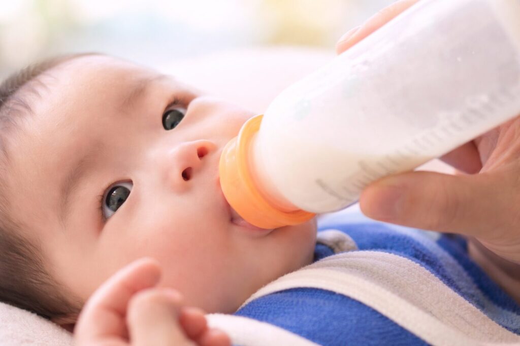 哺乳瓶でミルクを飲む赤ちゃんをやわらかい光で捉えた横長のイメージ写真