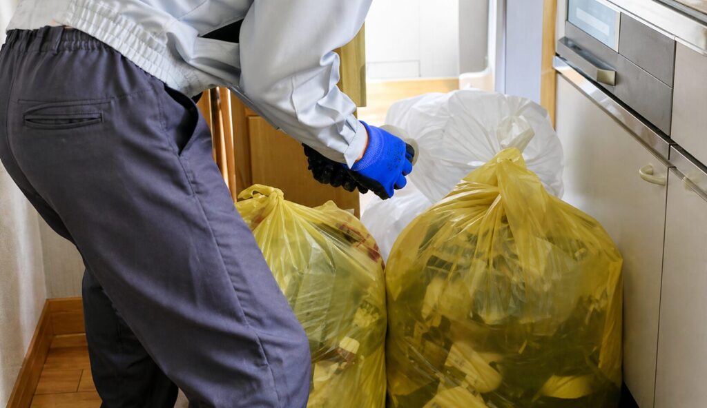 キッチンの通路で作業服の人物が手袋を着けてゴミ袋をまとめている様子