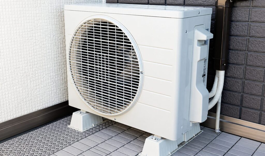 ベランダに設置された白いエアコン室外機の高解像度イメージで、配管や設置台座まで確認できる状態