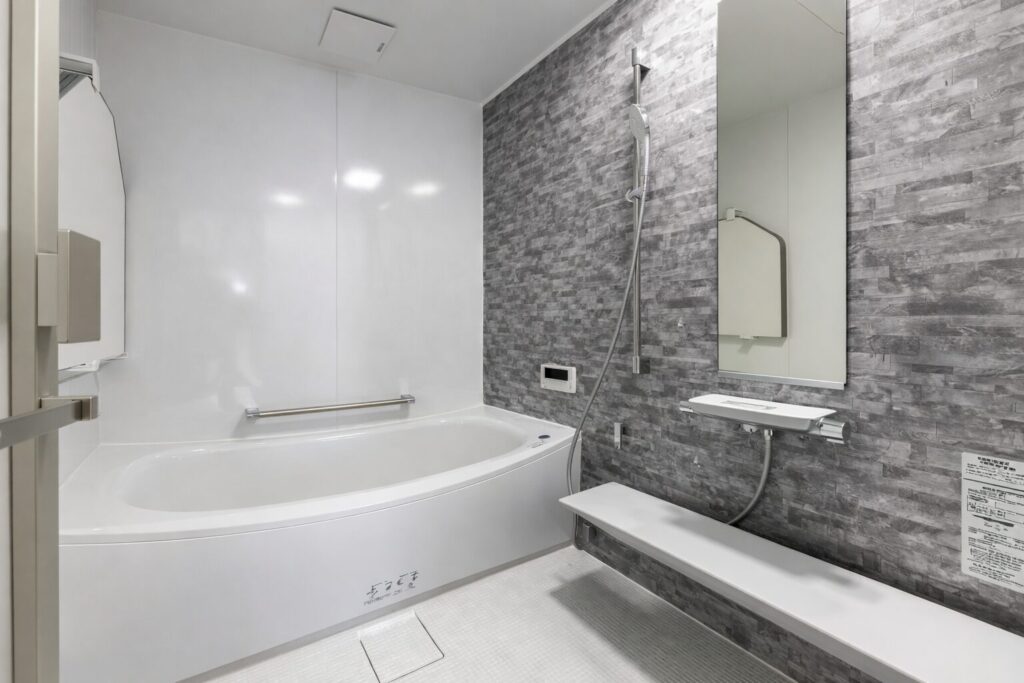 グレーのアクセント壁と白い浴槽が特徴的な、清潔感のあるユニットバスの室内空間