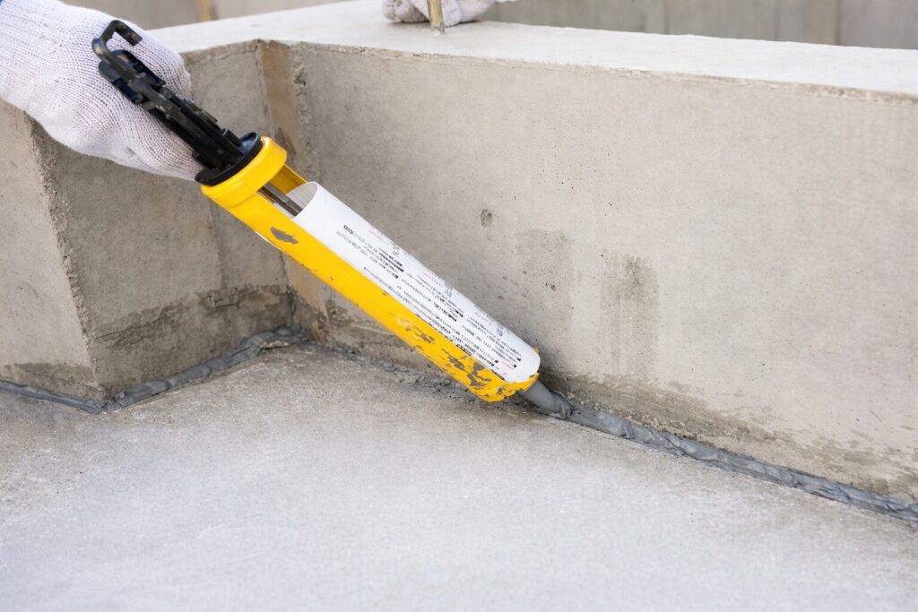 コンクリートの立ち上がりと床の継ぎ目にシーリング材を充填している作業風景（