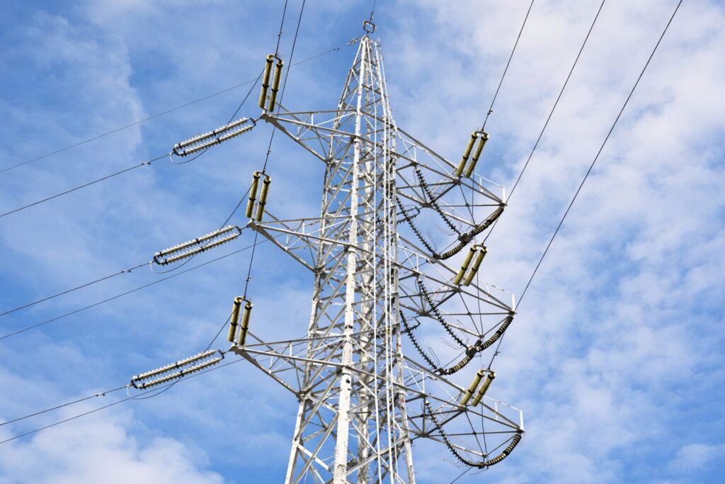 青空の下にそびえる高圧送電鉄塔と複数の電線、碍子がはっきりと見える構図