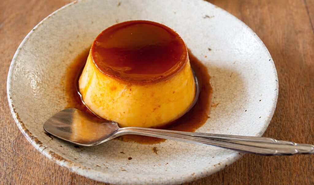 カラメルソースがたっぷりかかったプリンを皿にのせ、スプーンを添えたイメージ