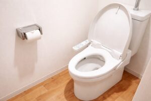 タンカーやコンテナ船、軍艦が行き交うホルムズ海峡を上空から俯瞰したイラストで、両岸には乾燥した山地と石油関連施設、沿岸の建物が描かれている