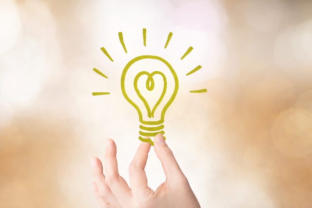 手の先に浮かぶハート型の光を放つ電球アイコンがひらめきを表現しているイメージ