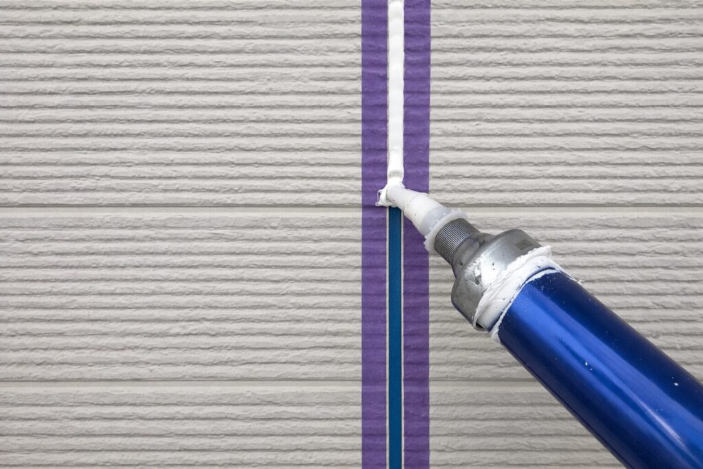 外壁の目地にマスキングテープを貼り、コーキングガンで白いシーリング材を充填している様子