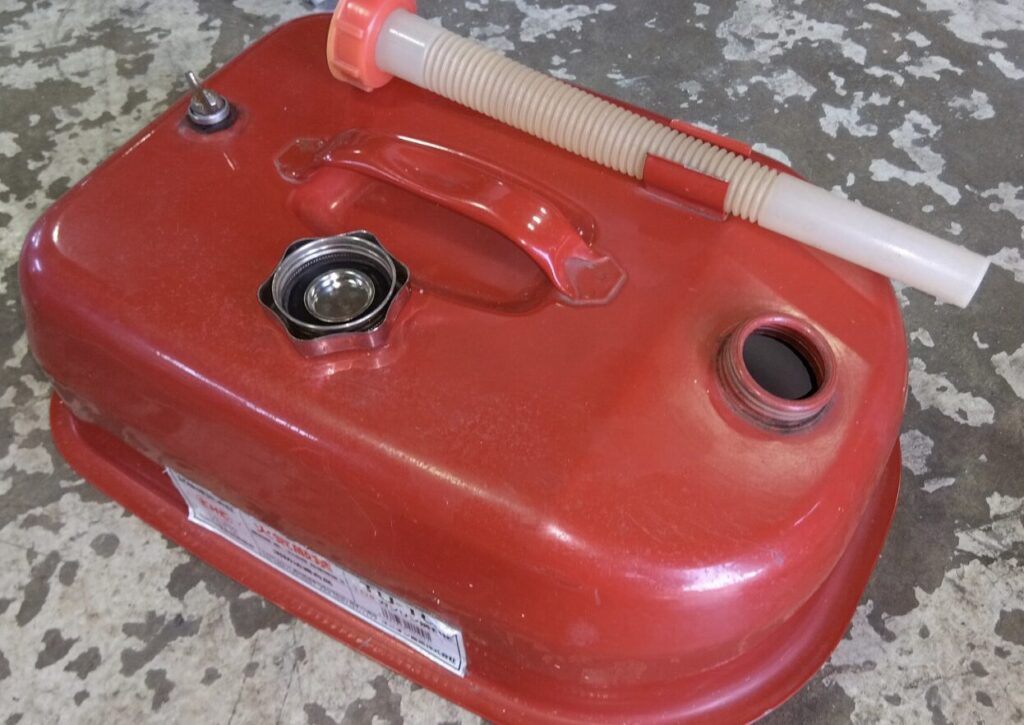赤い金属製のガソリン携行缶と給油ノズルがコンクリート床の上に置かれている様子