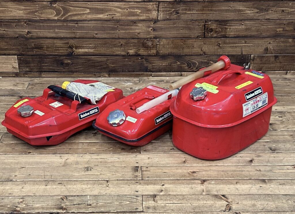 赤いガソリン携行缶が3つ並べられ、木目の背景の前に配置されている様子