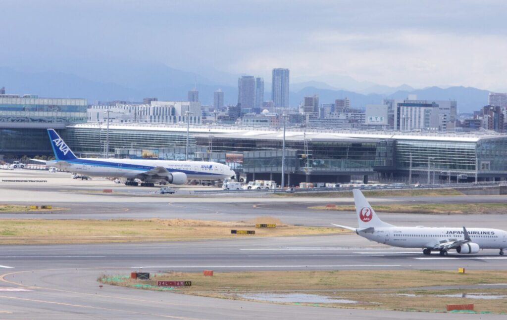 ジェット機が滑走路を走行し、空港ターミナル前に複数の旅客機が並ぶ様子を捉えた空港の風景