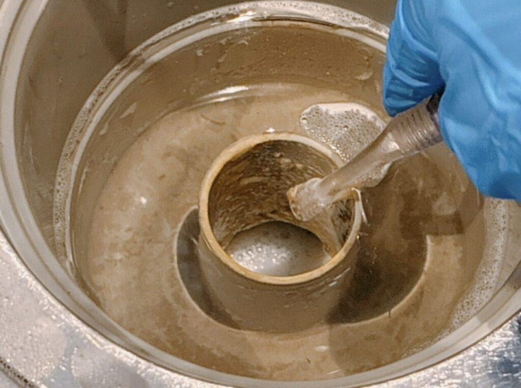 油汚れが付着した排水トラップ内部をブラシで清掃している様子